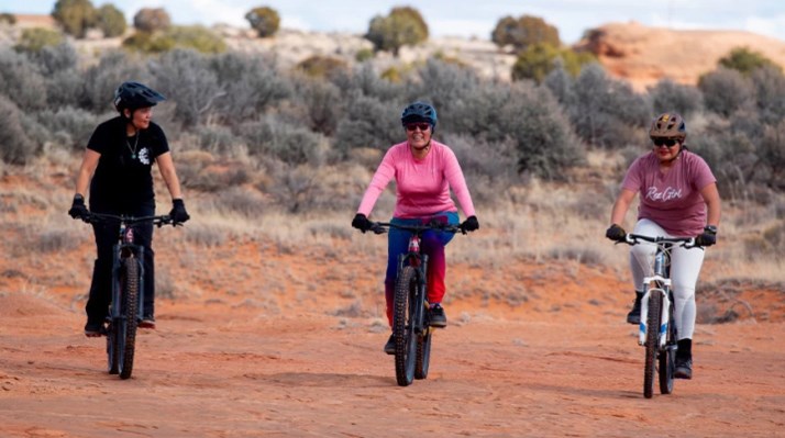 Three women riding Mountain bikes on a dirt trail.